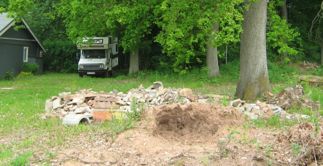 building rubble and an old tree stump with grass and a campervan in the distance